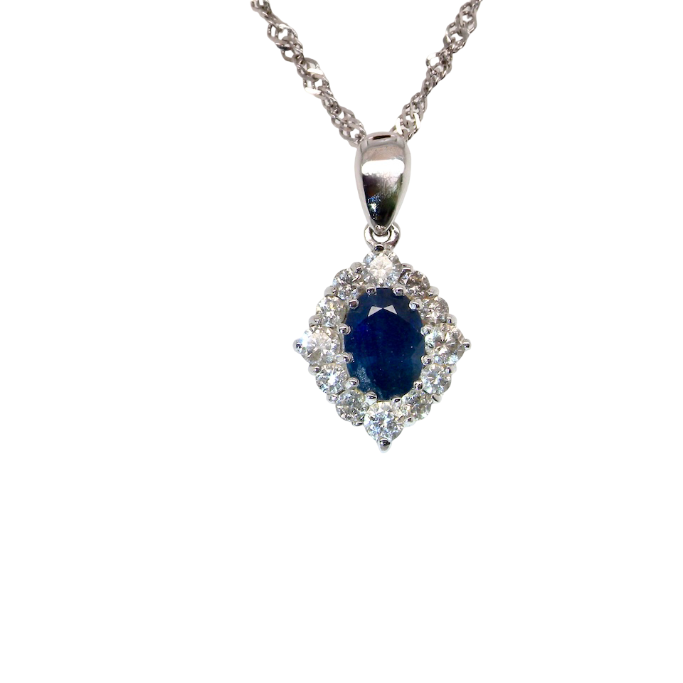 A white gold pendant. The centre stone an inky black blue sapphire 7x5mm, claw set. Complimented by an outer halo of twelve brilliant cut white diamonds.