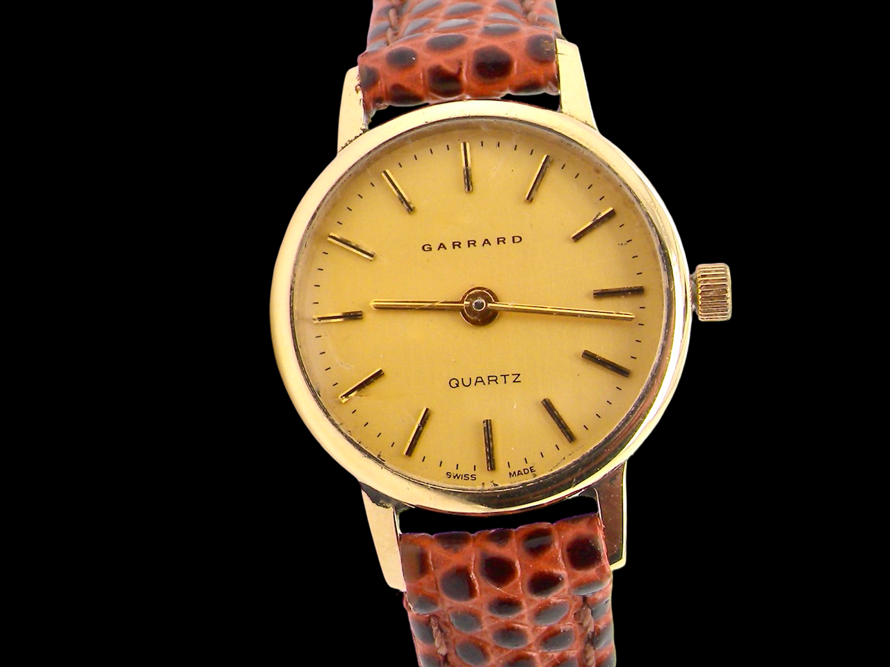 Garrard watch with gold face and brown leather strap on a black background