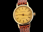 Garrard watch with gold face and brown leather strap on a black background
