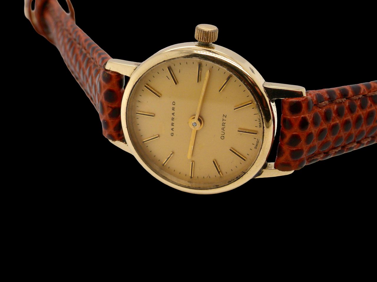 Wristwatch with a gold face and red lizard skin strap on a black background