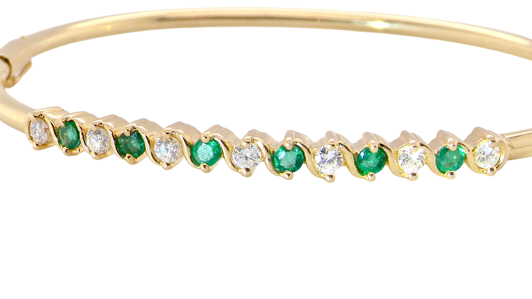 A yellow gold bangle. Features alternate emeralds and diamonds. Six 2.7mm emeralds and seven brilliant cut white diamonds, each 2.7mm