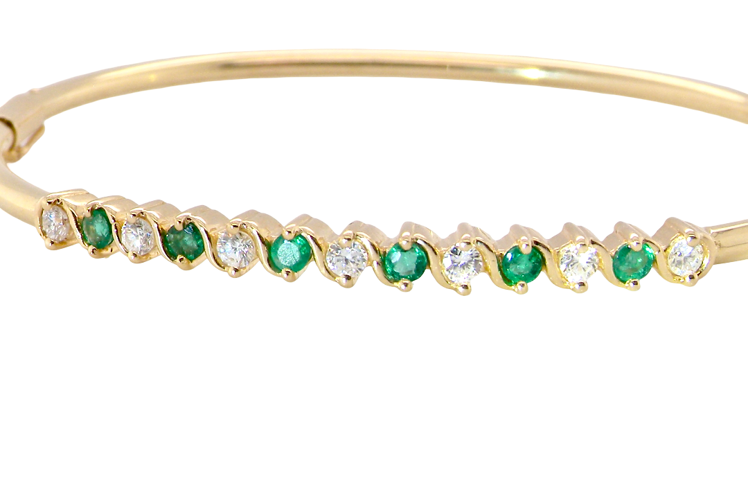 A yellow gold bangle. Features alternate emeralds and diamonds. Six 2.7mm emeralds and seven brilliant cut white diamonds, each 2.7mm
