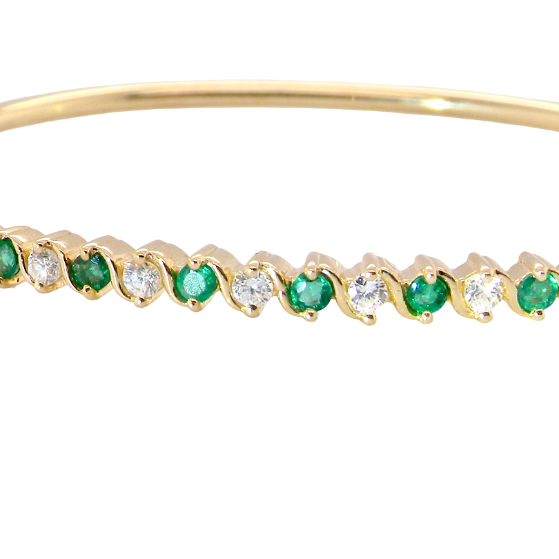 A yellow gold bangle. Features alternate emeralds and diamonds. Six 2.7mm emeralds and seven brilliant cut white diamonds, each 2.7mm