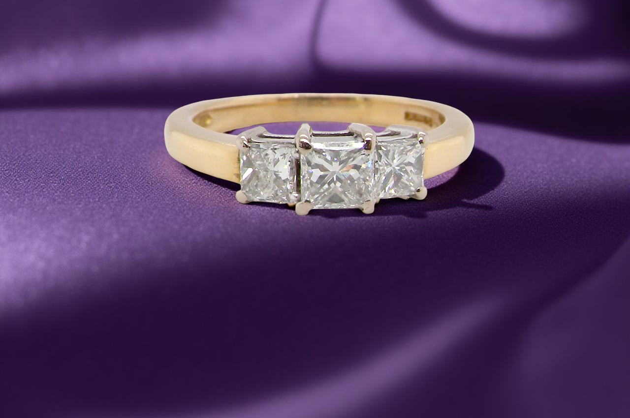 Gold ring with three diamonds on a purple fabric background