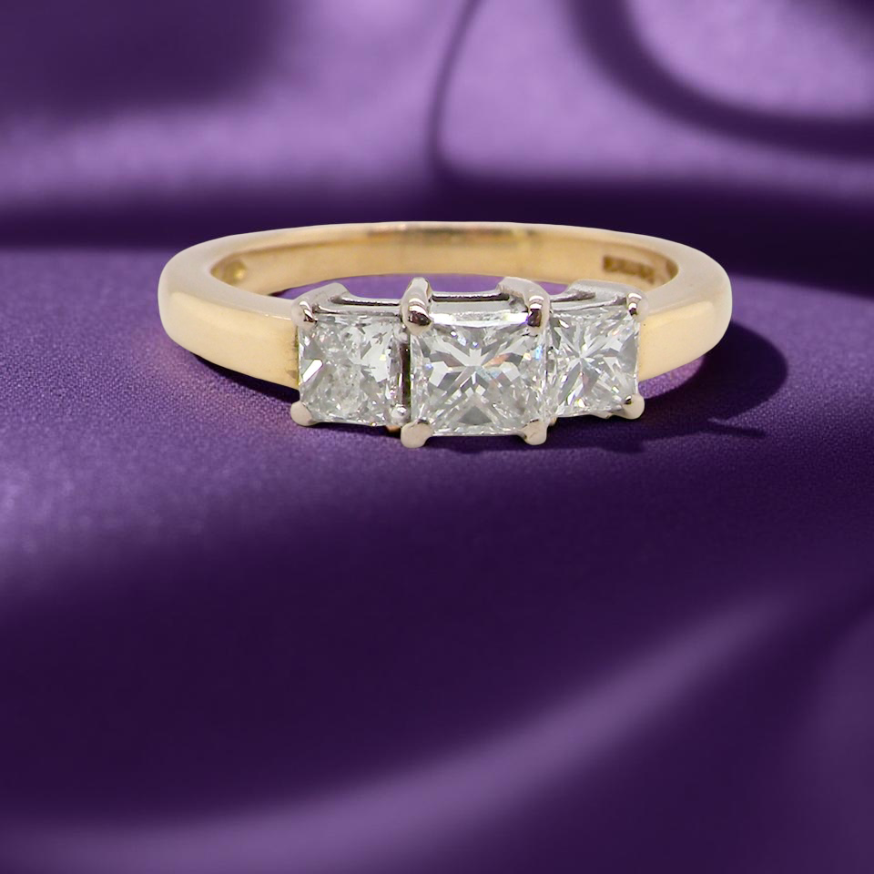 Gold ring with three diamonds on a purple fabric background