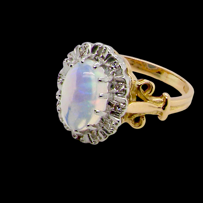 An 18 carat gold cluster ring. Features an oval opal centre stone with excellent play of colour with a predominance of watery purple and flashes of orange,
Measures 11x7mm.