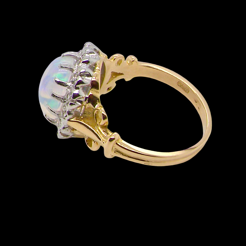 An 18 carat gold cluster ring. Features an oval opal centre stone with excellent play of colour with a predominance of watery purple and flashes of orange, luminous green.
Measures 11x7mm.