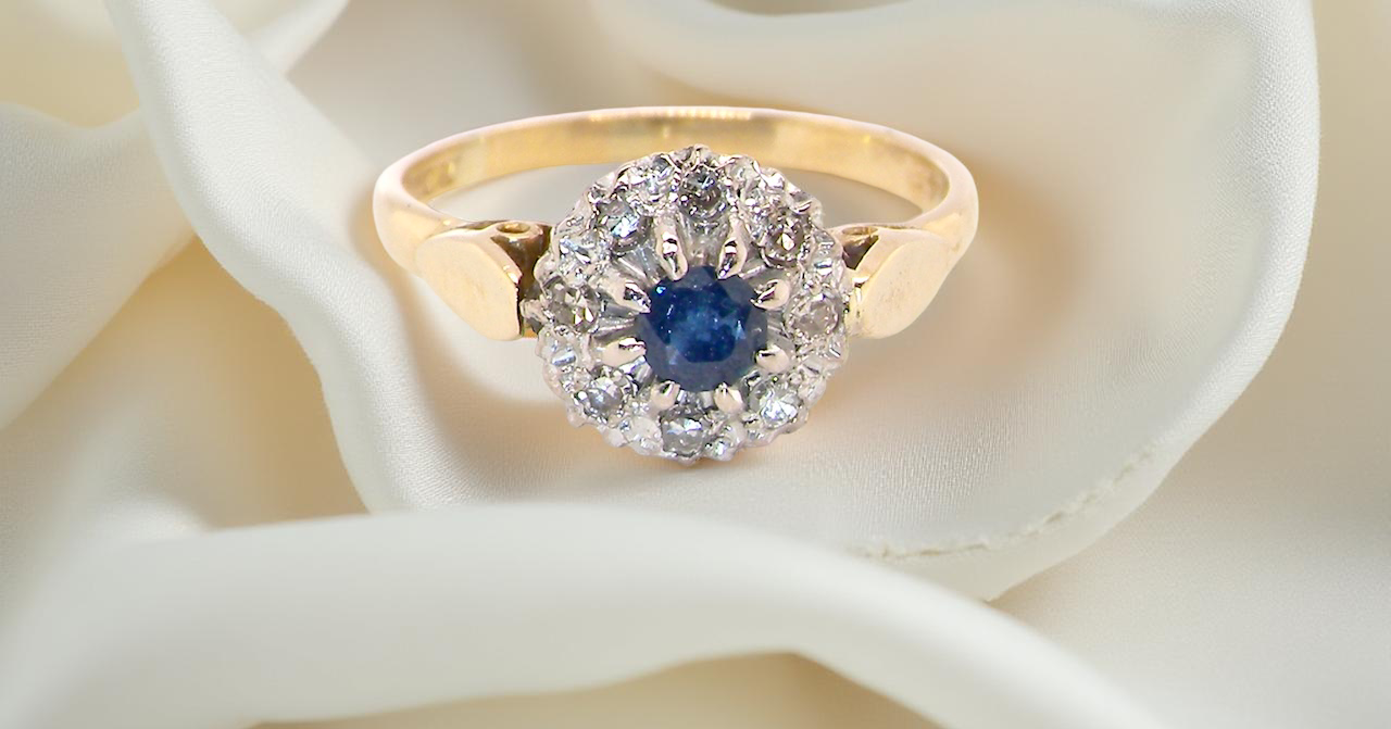 An 18 carat gold cluster ring, features to the centre a dark blue sapphire,