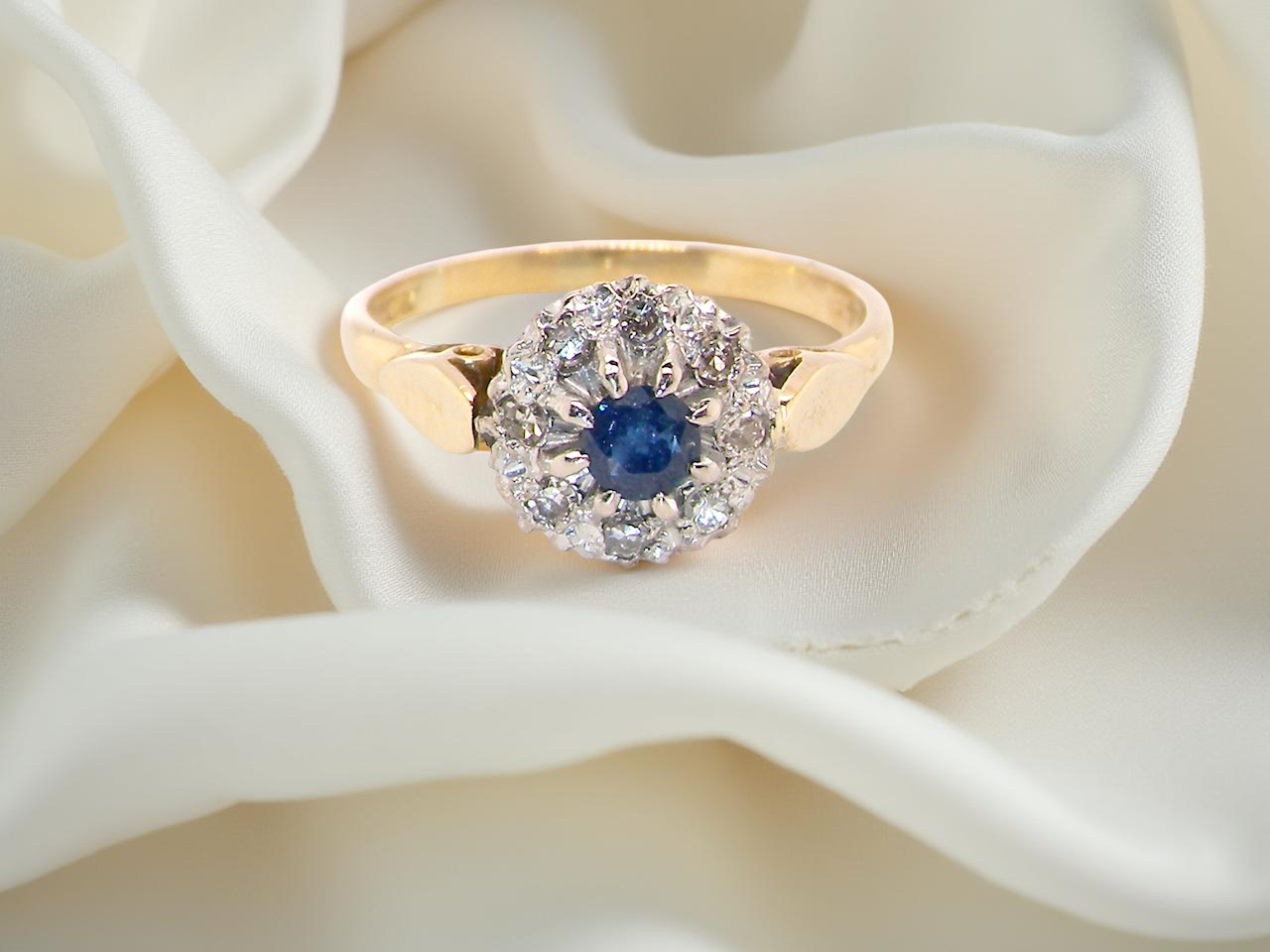 An 18 carat gold cluster ring, features to the centre a dark blue sapphire,