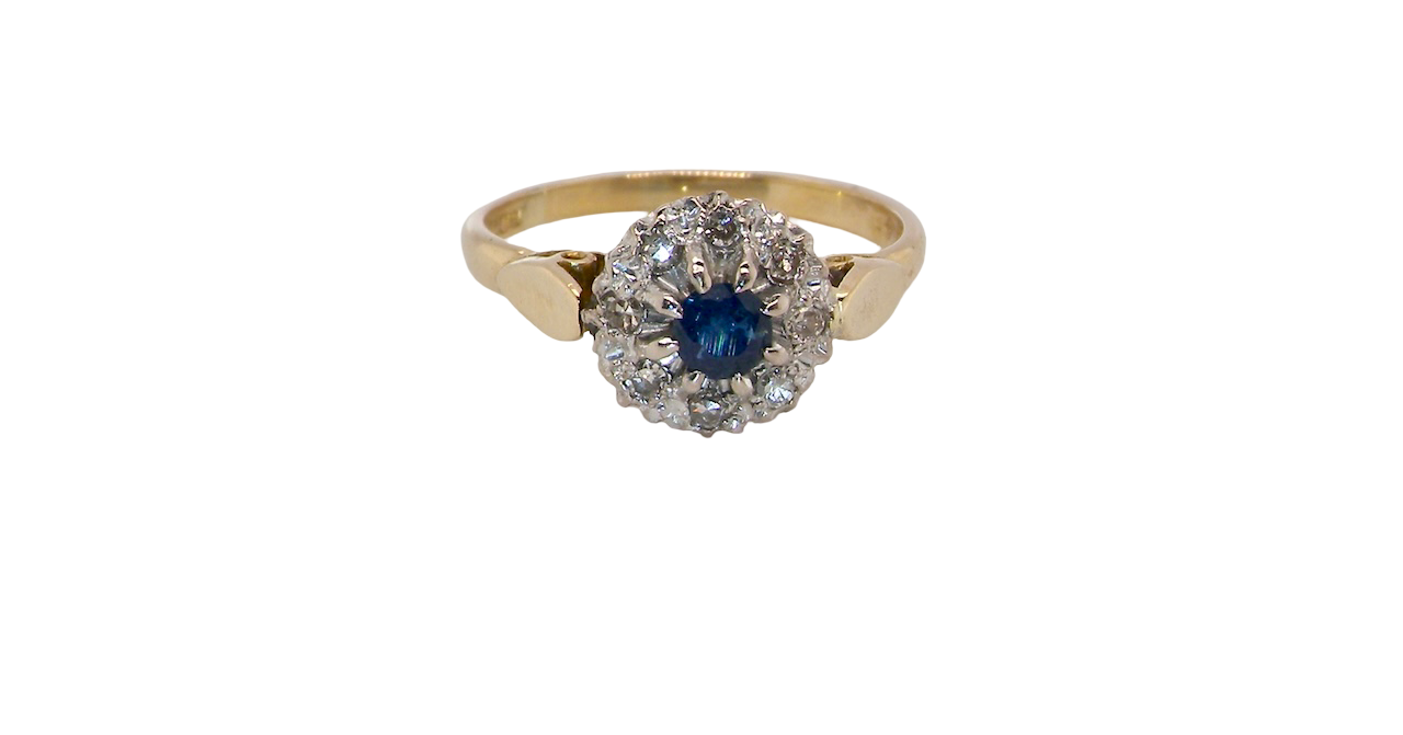 An 18 carat gold cluster ring, features to the centre a dark blue sapphire, 3.6mm diameter. Claw set.
