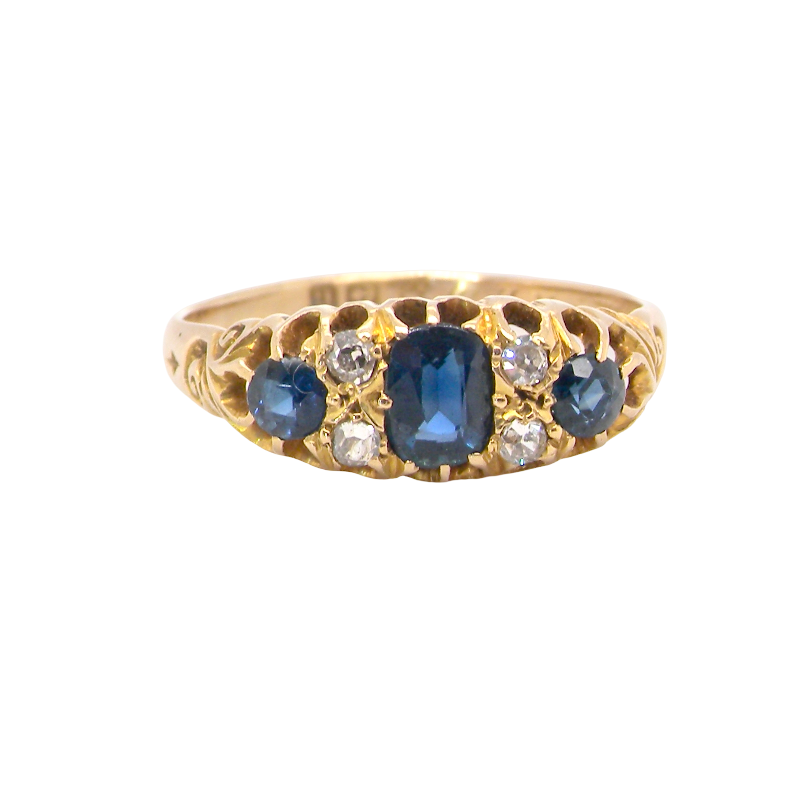 A vintage-style yellow gold ring featuring a central oval blue sapphire flanked by smaller round blue sapphires and clear round diamonds, set against a plain white background.