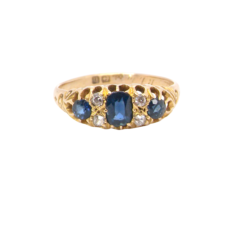 A yellow gold ring featuring a central oval-cut blue sapphire flanked by smaller round-cut blue sapphires and clear diamonds, set against a plain white background.