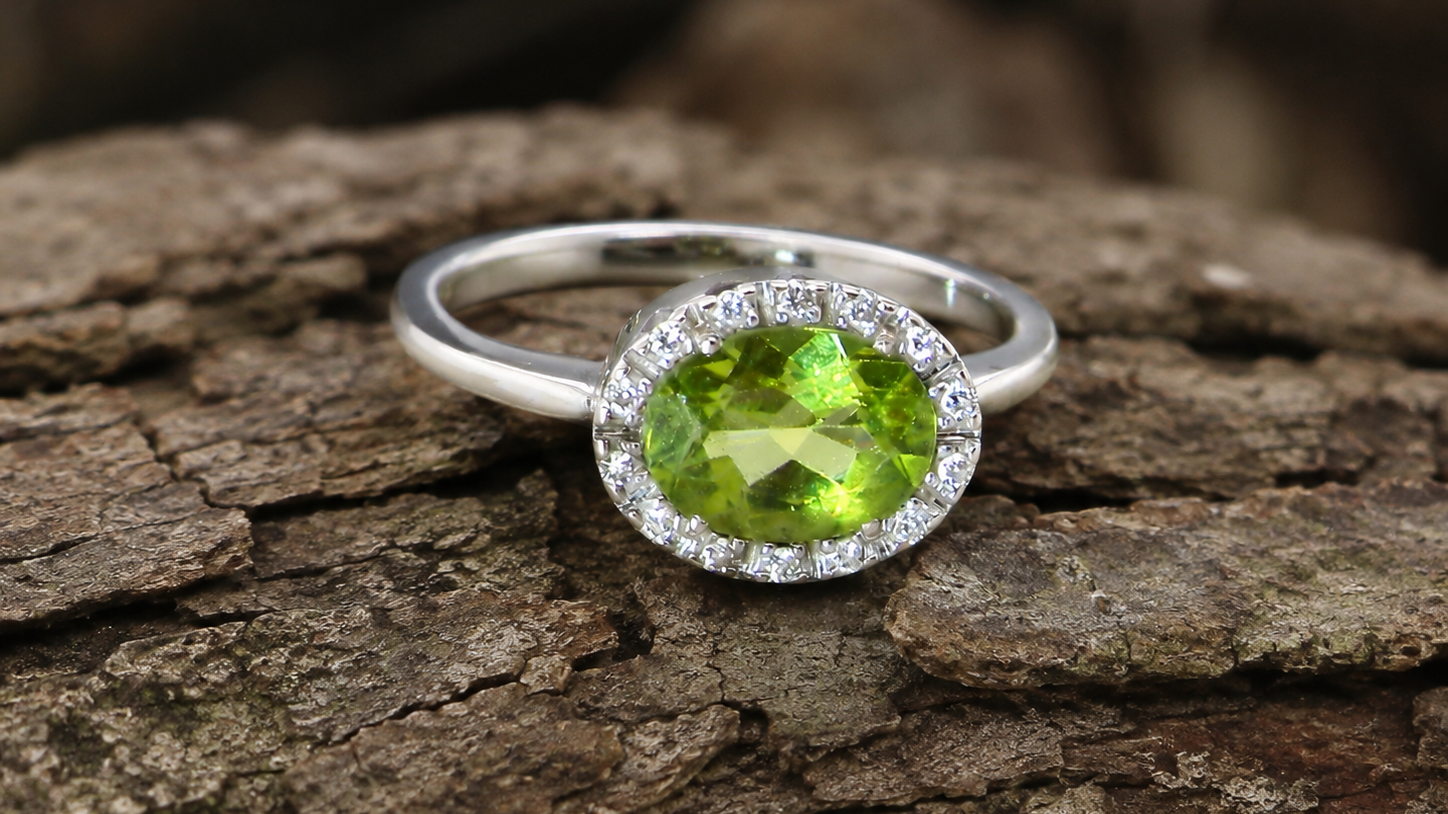 An 18 carat white gold* cluster ring. Features and oval shaped peridot measures 8.5x6.5mm.