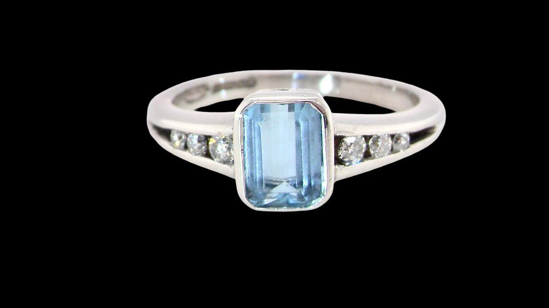 An 18 carat white gold ring, features a rectangular step cut aquamarine, measures 7x5mm (st one carat) , fine clarity. Rim setting.