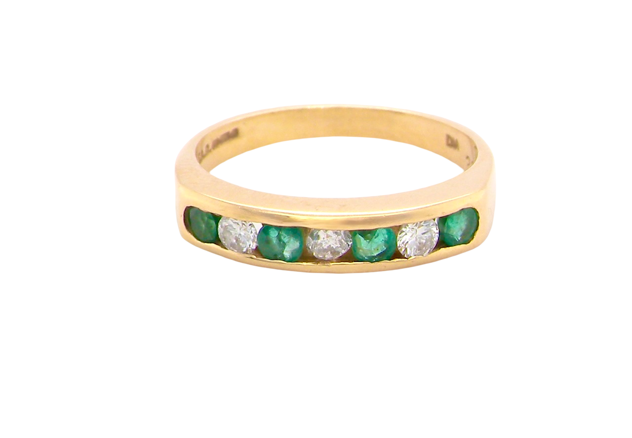 An 18 carat yellow gold half hoop eternity ring. Set with four round emeralds, each 3mm, and alternate set with brilliant cut white diamonds, each 3mm