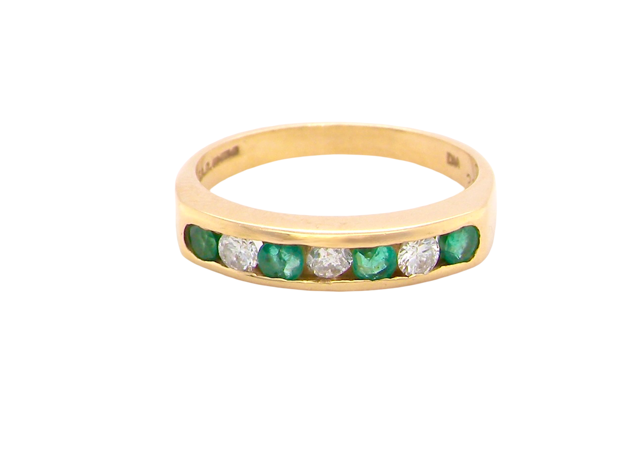 An 18 carat yellow gold half hoop eternity ring. Set with four round emeralds, each 3mm, and alternate set with brilliant cut white diamonds, each 3mm