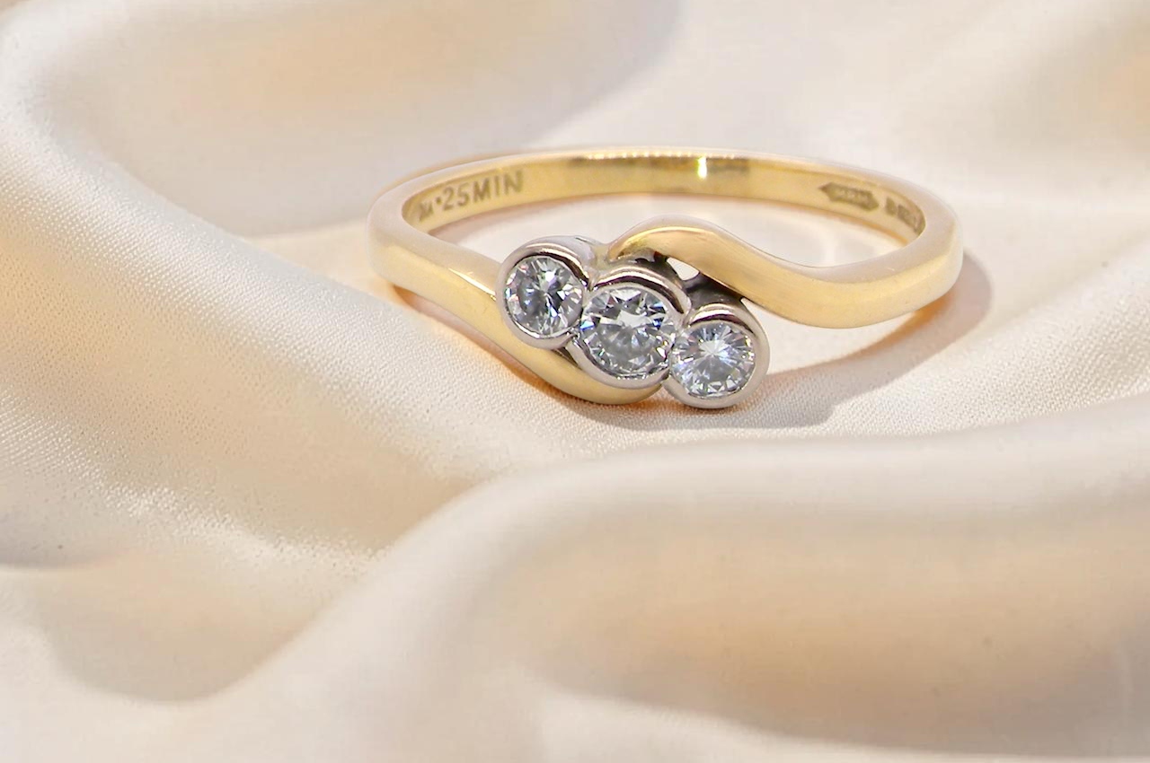 An 18 carat yellow gold three stone ring, cross over style, and set with brilliant cut white diamonds.
Centre stone 3mm