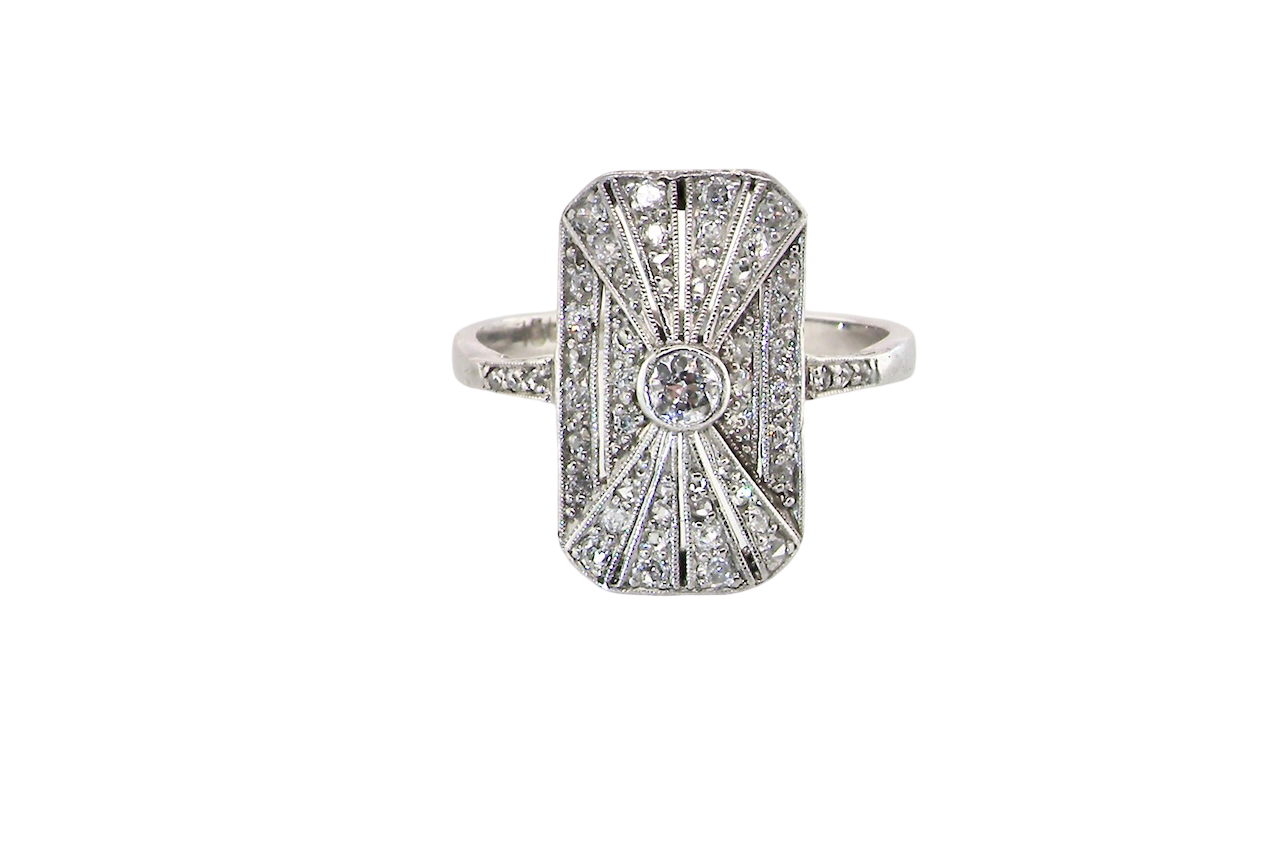 An Art Deco panel shaped cluster ring. The head measures 16x10mm, depth 3.4mm, and has two fan shaped designs that feature above and below a brilliant cut white diamond centre stone which measures 3.4mm (0.15 carats est)