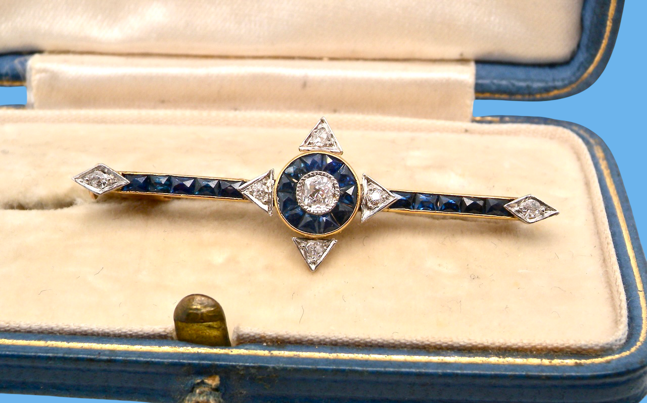 An Edwardian bar brooch. The centre 'target' style portion is set with a brilliant cut white diamond 4mm (0.25 carats) colour H-j, . Mille grain setting.