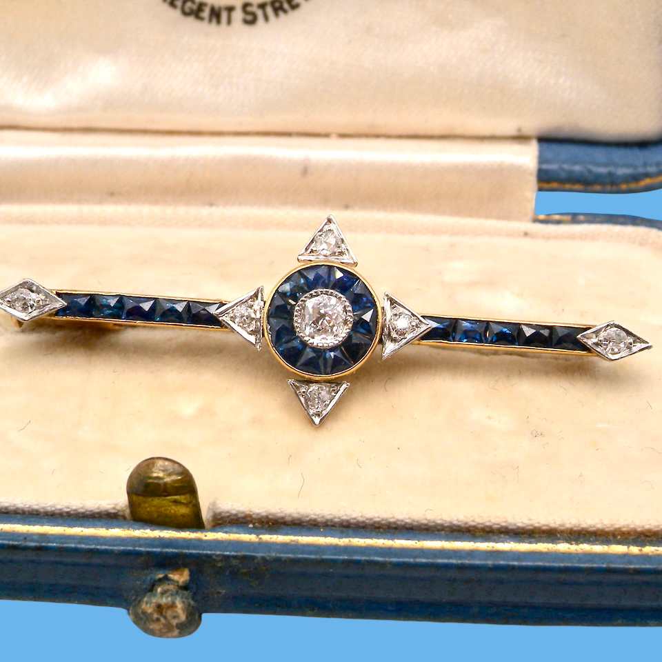 An Edwardian bar brooch. The centre 'target' style portion is set with a brilliant cut white diamond 4mm (0.25 carats) colour H-j, . Mille grain setting.
