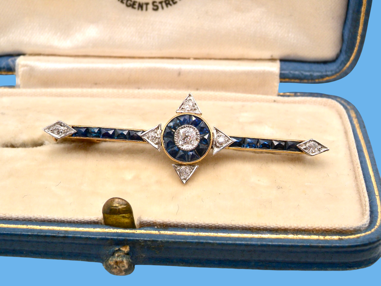 An Edwardian bar brooch. The centre 'target' style portion is set with a brilliant cut white diamond 4mm (0.25 carats) colour H-j, . Mille grain setting.
