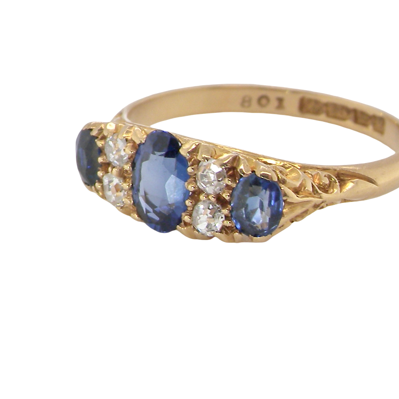 A vintage yellow gold ring featuring three oval blue sapphires and small round clear diamonds, shown on a plain white background. The inside of the band is stamped with '9K 18M GOLD'.