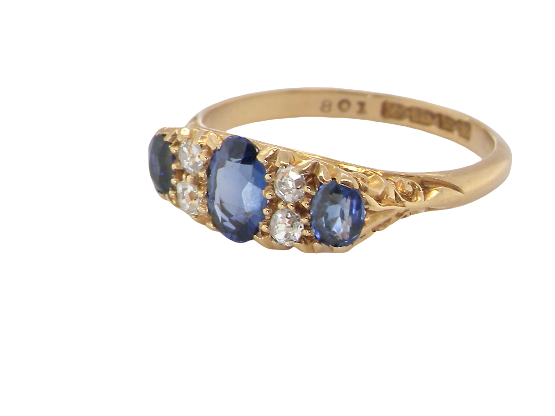 A vintage yellow gold ring featuring three oval blue sapphires and small round clear diamonds, shown on a plain white background. The inside of the band is stamped with '9K 18M GOLD'.
