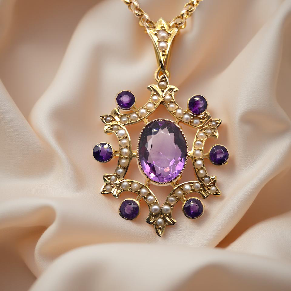 Gold pendant with purple gemstone on a beige fabric background
