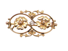 Gold brooch with floral designs and a central gemstone on a white background