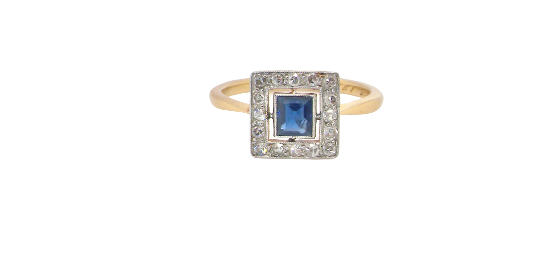 An early 20th century square cluster ring. Features a square inky black blue sapphire, 4x4mm (est 0.25 carats) mille grain set.
Complimented by an outer border of small old cut white diamonds, each 1.7mm (est total 0.30 carats) . The head tests as platinum 9.3x9.3mm, depth 3.8mm. Weight 2.4grams.
Pretty gold under setting, band stamped 18CT PLAT, a