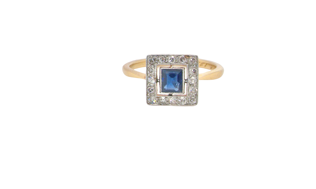 An early 20th century square cluster ring. Features a square inky black blue sapphire, 4x4mm (est 0.25 carats) mille grain set.
Complimented by an outer border of small old cut white diamonds, each 1.7mm (est total 0.30 carats) . The head tests as platinum 9.3x9.3mm, depth 3.8mm. Weight 2.4grams.
Pretty gold under setting, band stamped 18CT PLAT, a