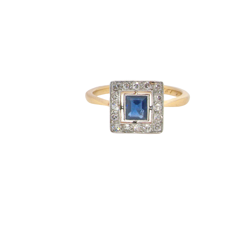 An early 20th century square cluster ring. Features a square inky black blue sapphire, 4x4mm (est 0.25 carats) mille grain set.
Complimented by an outer border of small old cut white diamonds, each 1.7mm (est total 0.30 carats) . The head tests as platinum 9.3x9.3mm, depth 3.8mm. Weight 2.4grams.
Pretty gold under setting, band stamped 18CT PLAT, a