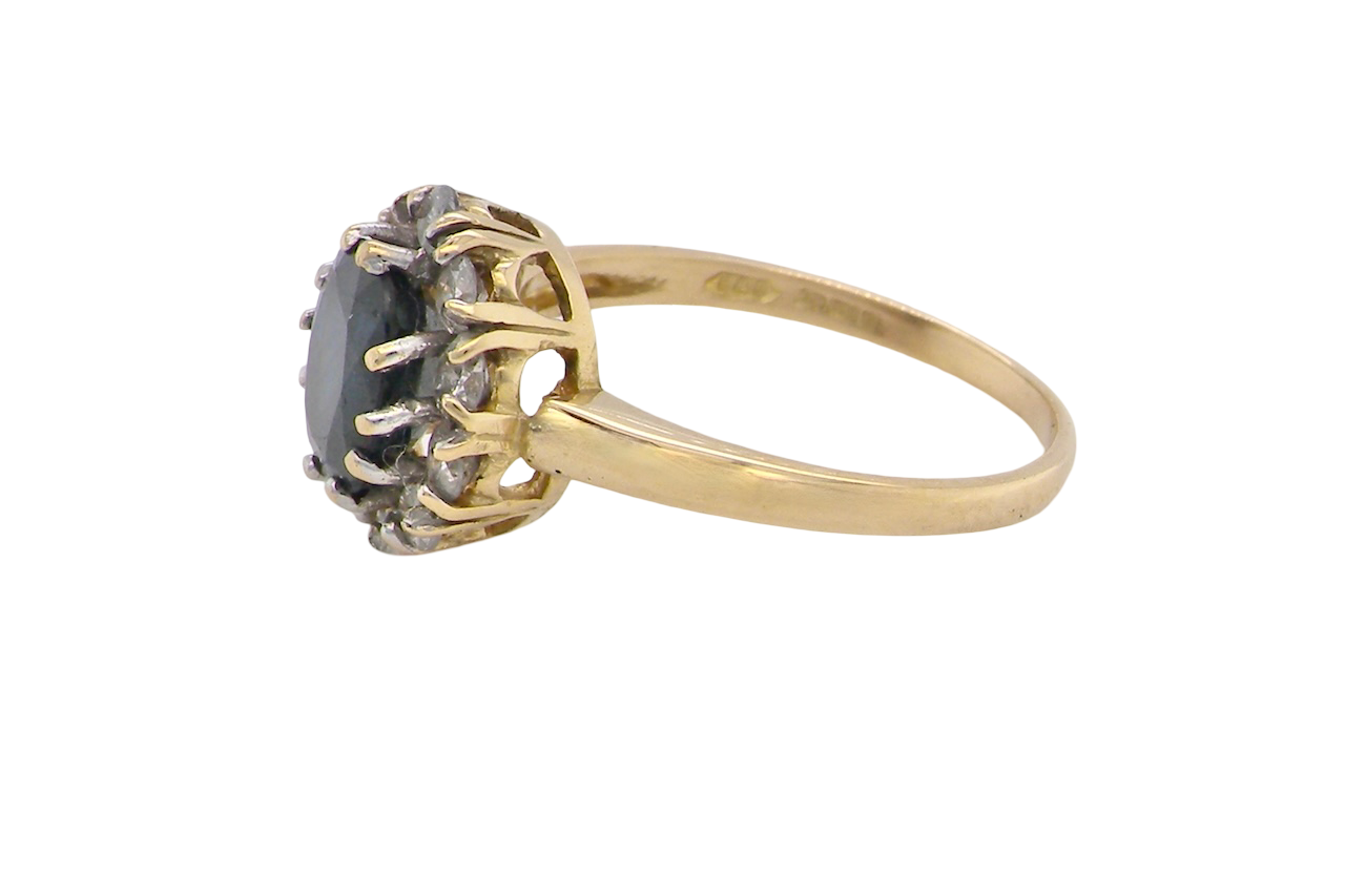 A An elegant 18 carat gold cluster ring featuring a striking inky dark blue sapphire at its centre.