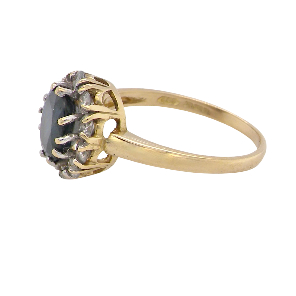 A An elegant 18 carat gold cluster ring featuring a striking inky dark blue sapphire at its centre.
