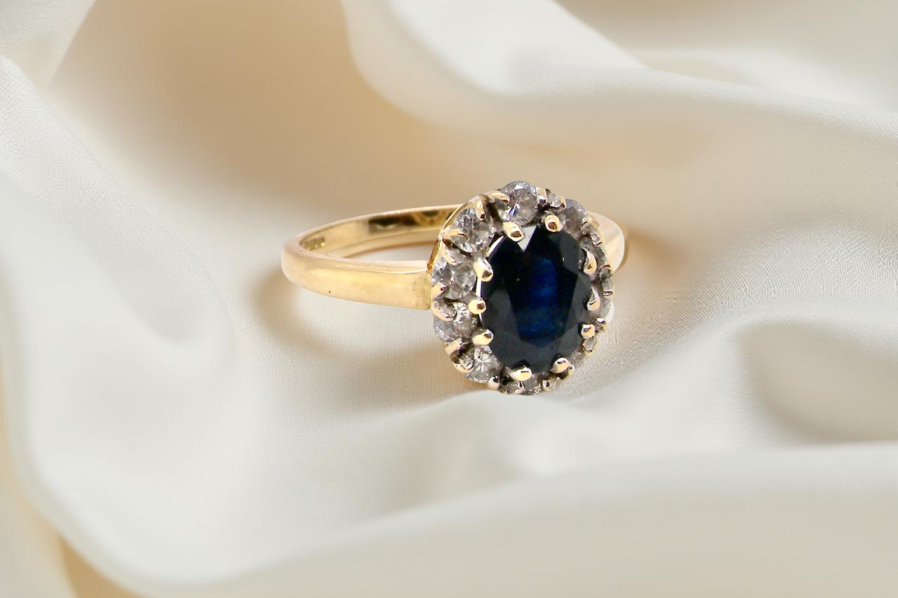 An elegant 18 carat gold cluster ring featuring a striking inky dark blue sapphire at its centre. B