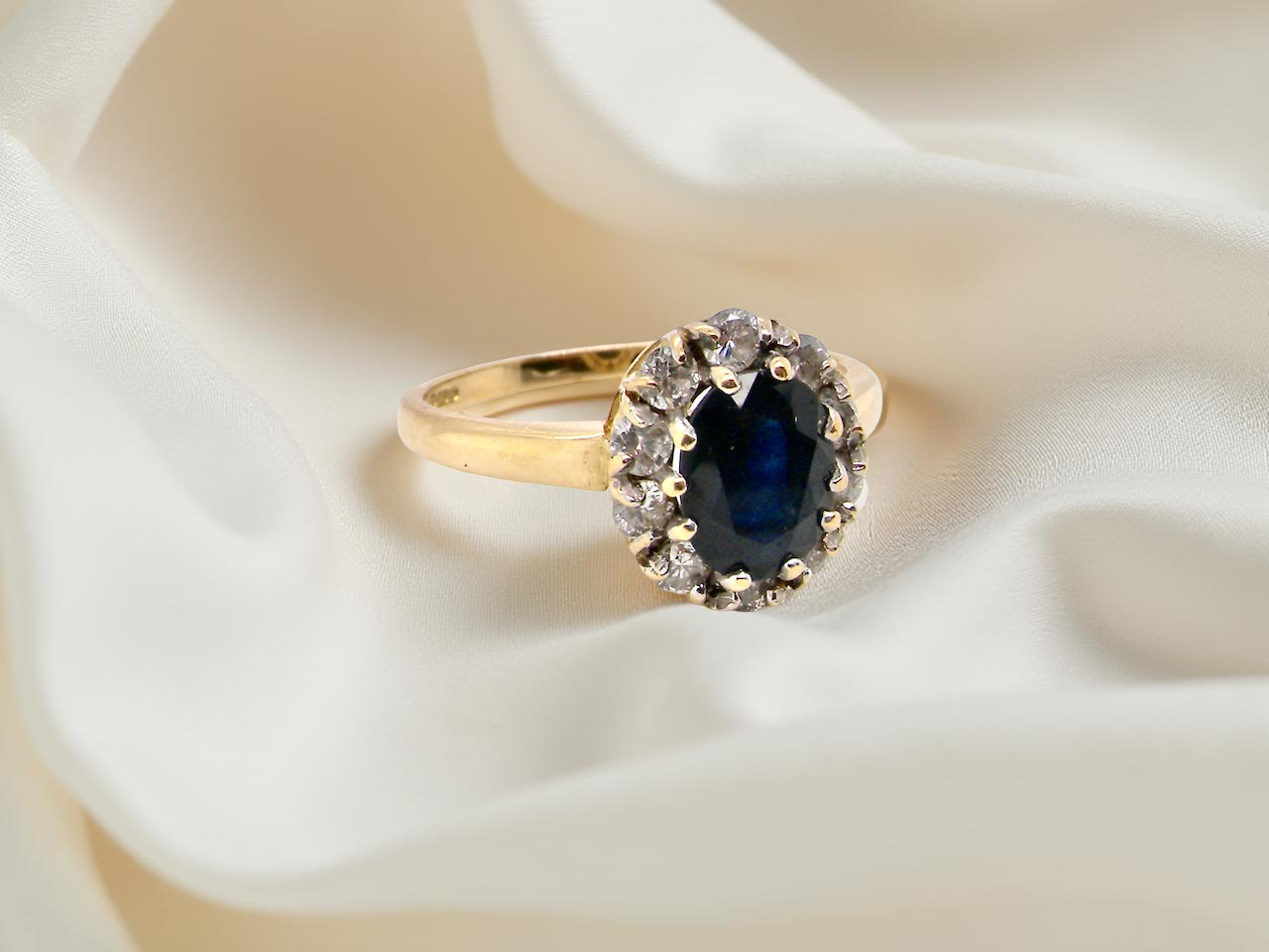 An elegant 18 carat gold cluster ring featuring a striking inky dark blue sapphire at its centre. B