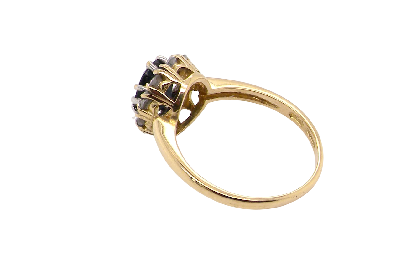 side An elegant 18 carat gold cluster ring featuring a striking inky dark blue sapphire at its centre.
