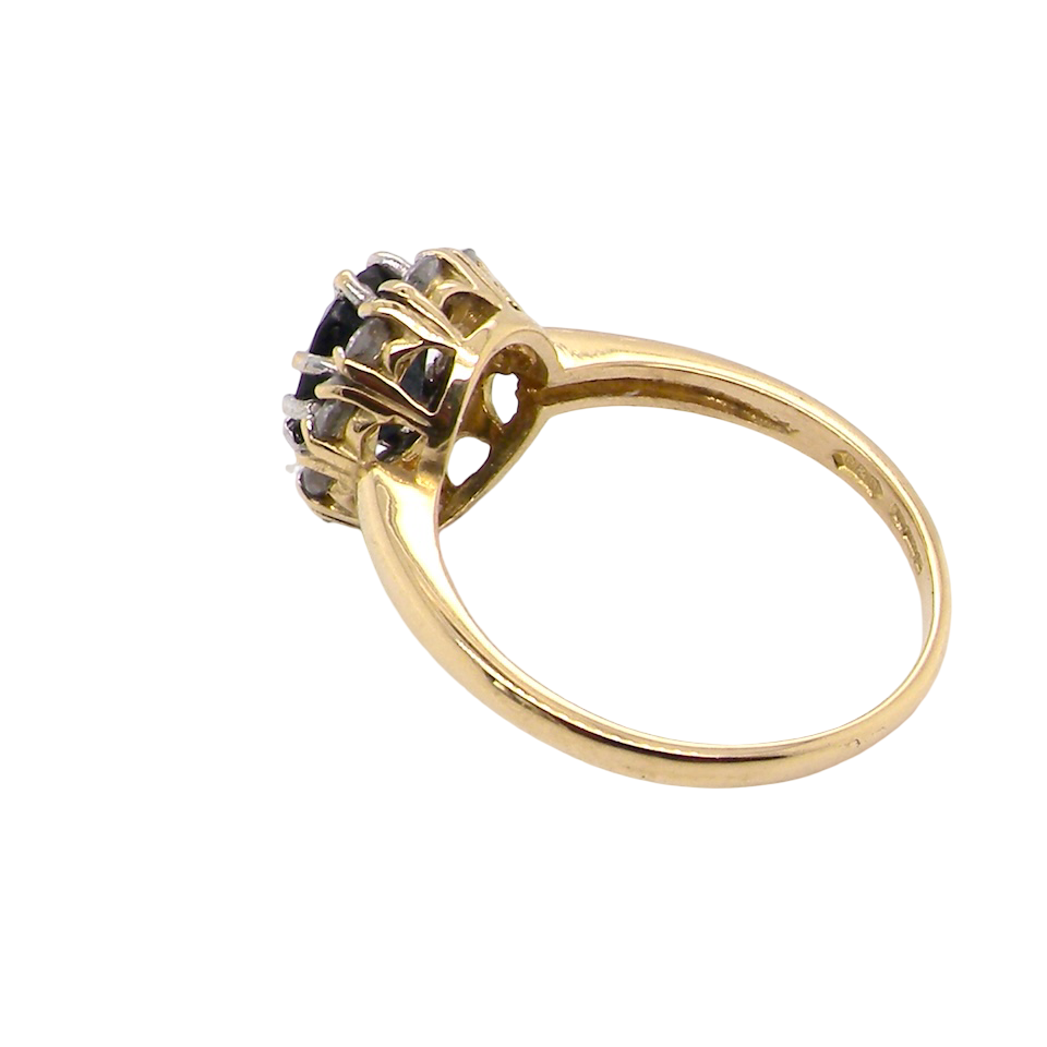 side An elegant 18 carat gold cluster ring featuring a striking inky dark blue sapphire at its centre.