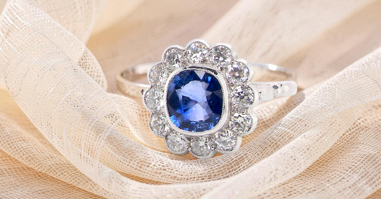 An elegant and timeless cluster ring, centrally set with a beautiful mid to deep blue cushion-cut sapphire,