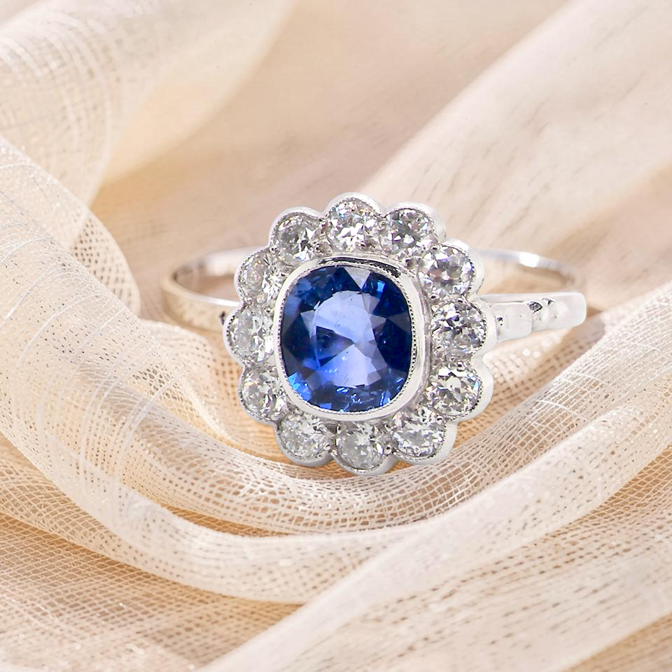 An elegant and timeless cluster ring, centrally set with a beautiful mid to deep blue cushion-cut sapphire,