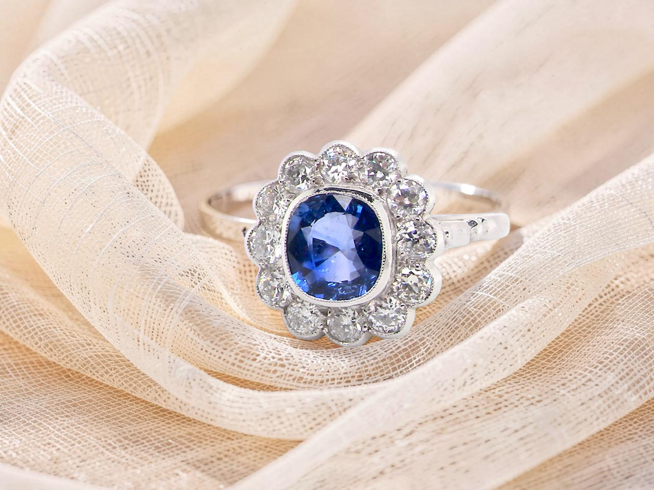 An elegant and timeless cluster ring, centrally set with a beautiful mid to deep blue cushion-cut sapphire,
