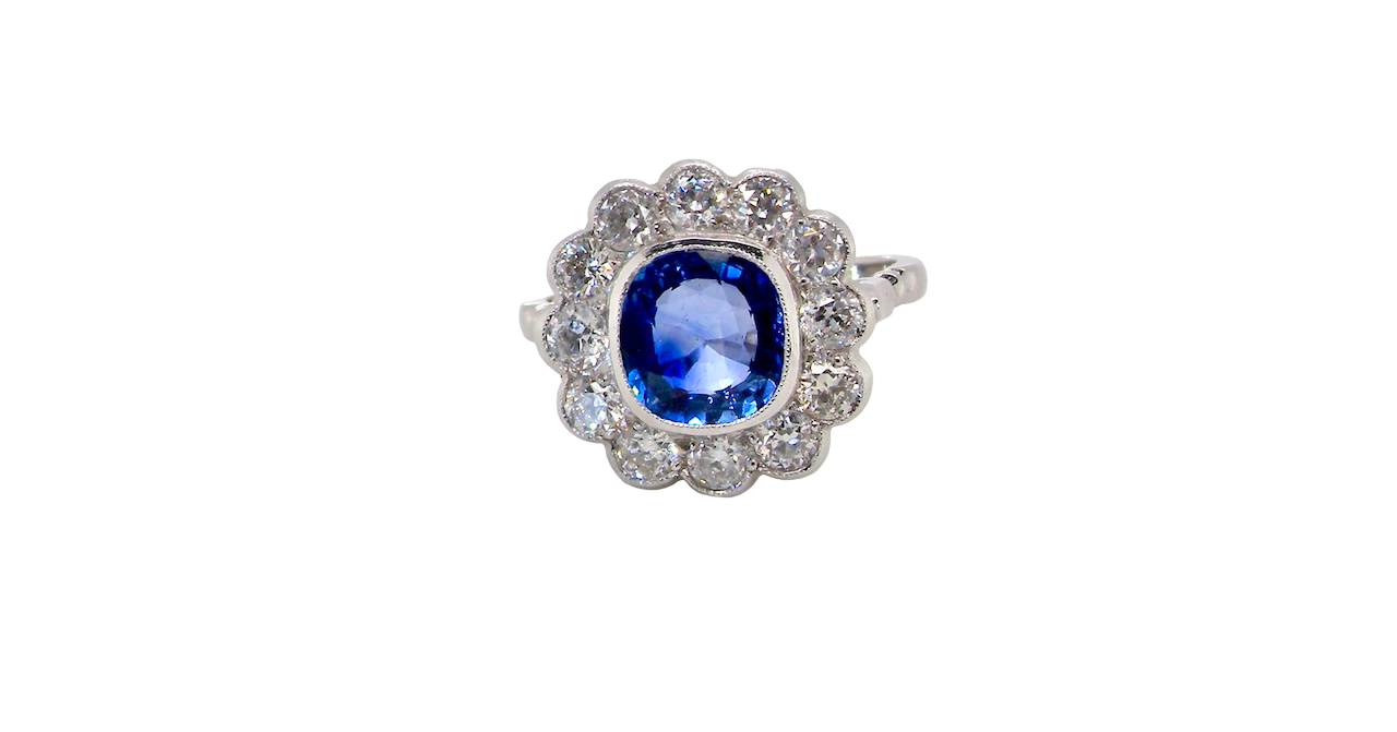 An elegant and timeless cluster ring, centrally set with a beautiful mid to deep blue cushion-cut sapphire, measuring approximately 8 x 8mm (estimated 2.00 carats).