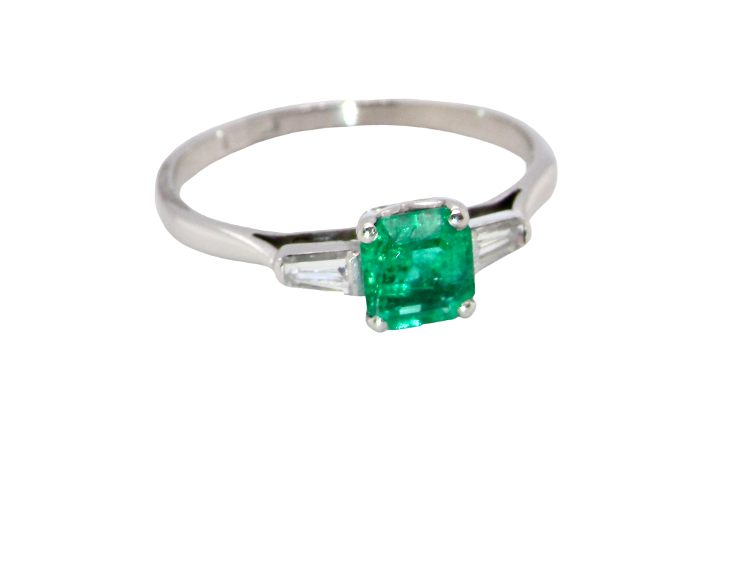 An elegant and timeless platinum ring featuring a stunning step-cut emerald to the centre, measuring approximately 5.5 x 5.5mm and estimated at 0.80 carats. The emerald displays a deep green colour with excellent presence.