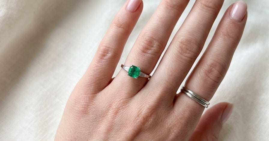 An elegant platinum ring featuring a stunning step-cut emerald to the centre, measuring approximately 5.5 x 5.5mm and estimated at 0.80 carats. The emerald displays a vibrant, deep green colour with excellent presence.