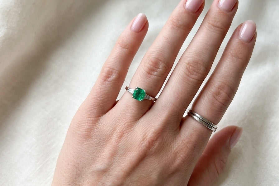 An elegant platinum ring featuring a stunning step-cut emerald to the centre, measuring approximately 5.5 x 5.5mm and estimated at 0.80 carats. The emerald displays a vibrant, deep green colour with excellent presence.