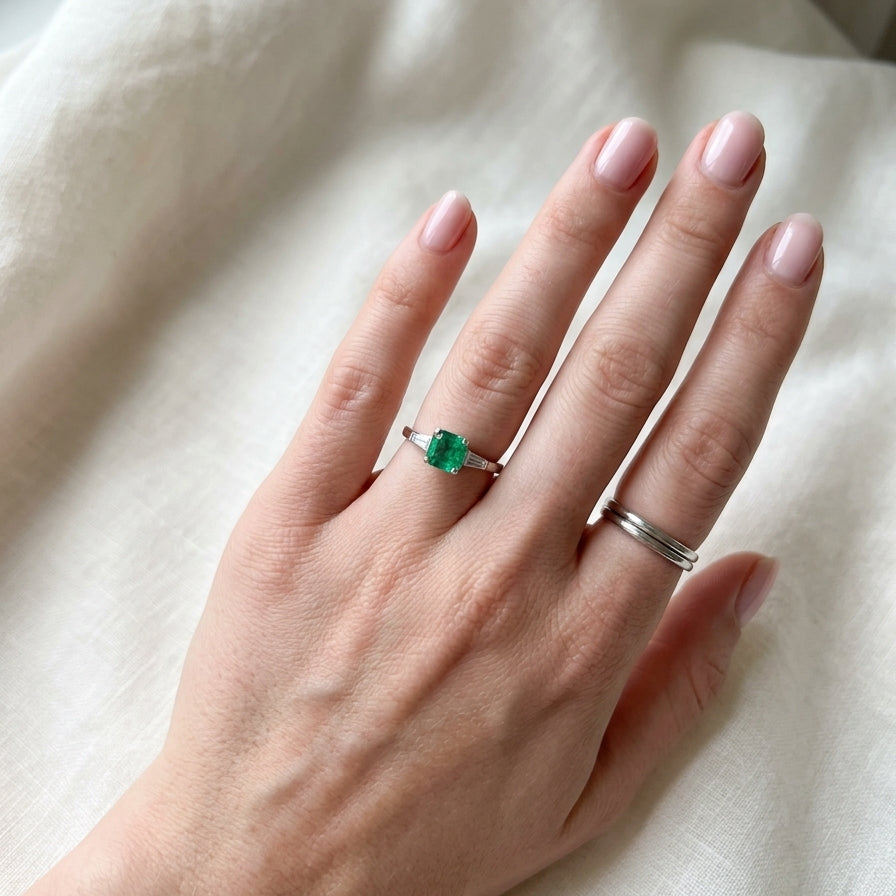 An elegant platinum ring featuring a stunning step-cut emerald to the centre, measuring approximately 5.5 x 5.5mm and estimated at 0.80 carats. The emerald displays a vibrant, deep green colour with excellent presence.
