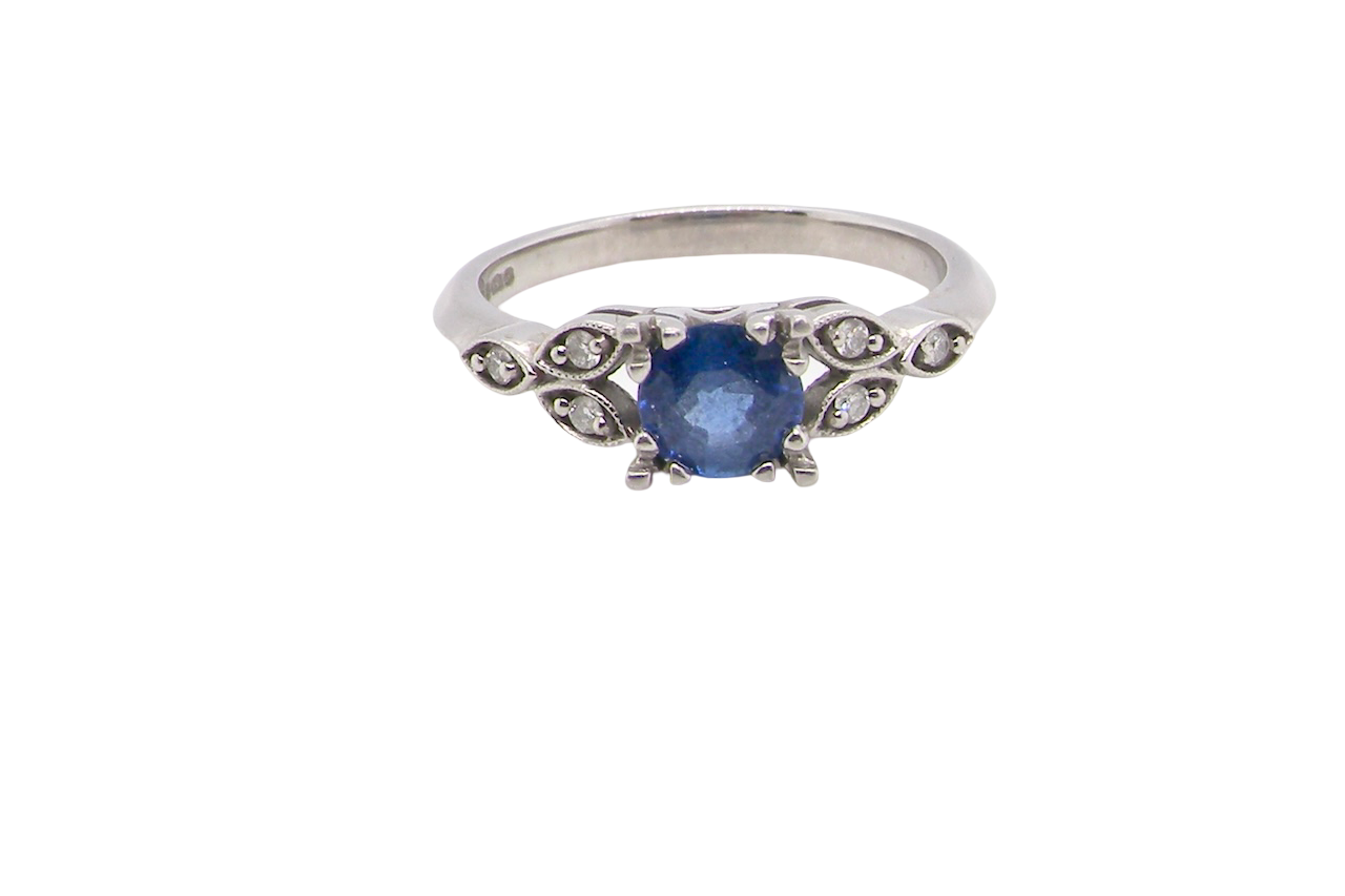 An elegant vintage-style platinum ring showcasing a beautifully proportioned round sapphire with a soft mid to light cornflower blue hue. The sapphire measures 5.6mm in diameter (approx. 0.80 carats)