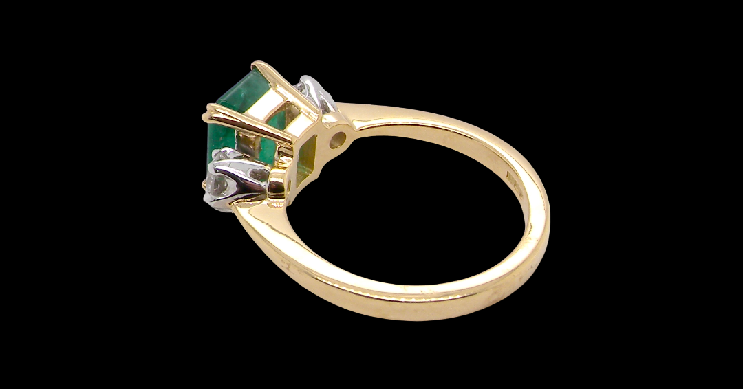 An exceptional three-stone ring featuring a vibrant step-cut emerald to the centre, measuring 8.6 x 7.0mm and weighing approximately 2.10 carats. The emerald displays a beautiful grass-green colour and is secured in a classic setting.