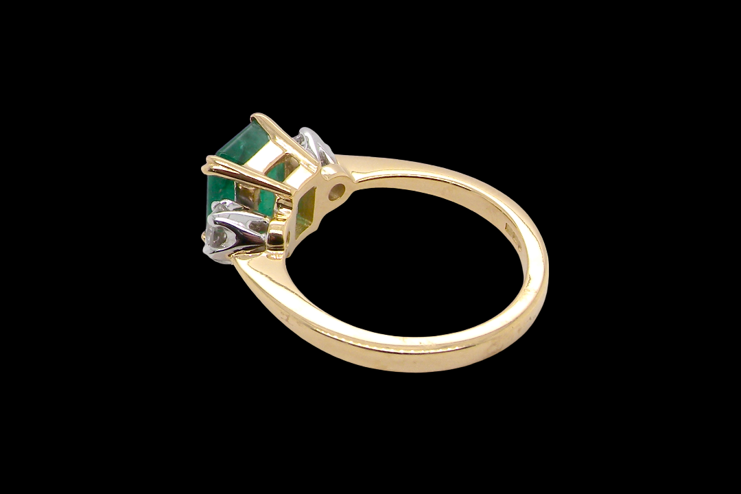An exceptional three-stone ring featuring a vibrant step-cut emerald to the centre, measuring 8.6 x 7.0mm and weighing approximately 2.10 carats. The emerald displays a beautiful grass-green colour and is secured in a classic setting.