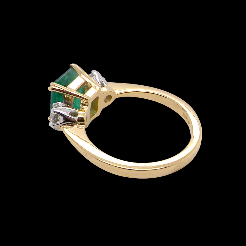An exceptional three-stone ring featuring a vibrant step-cut emerald to the centre, measuring 8.6 x 7.0mm and weighing approximately 2.10 carats. The emerald displays a beautiful grass-green colour and is secured in a classic setting.